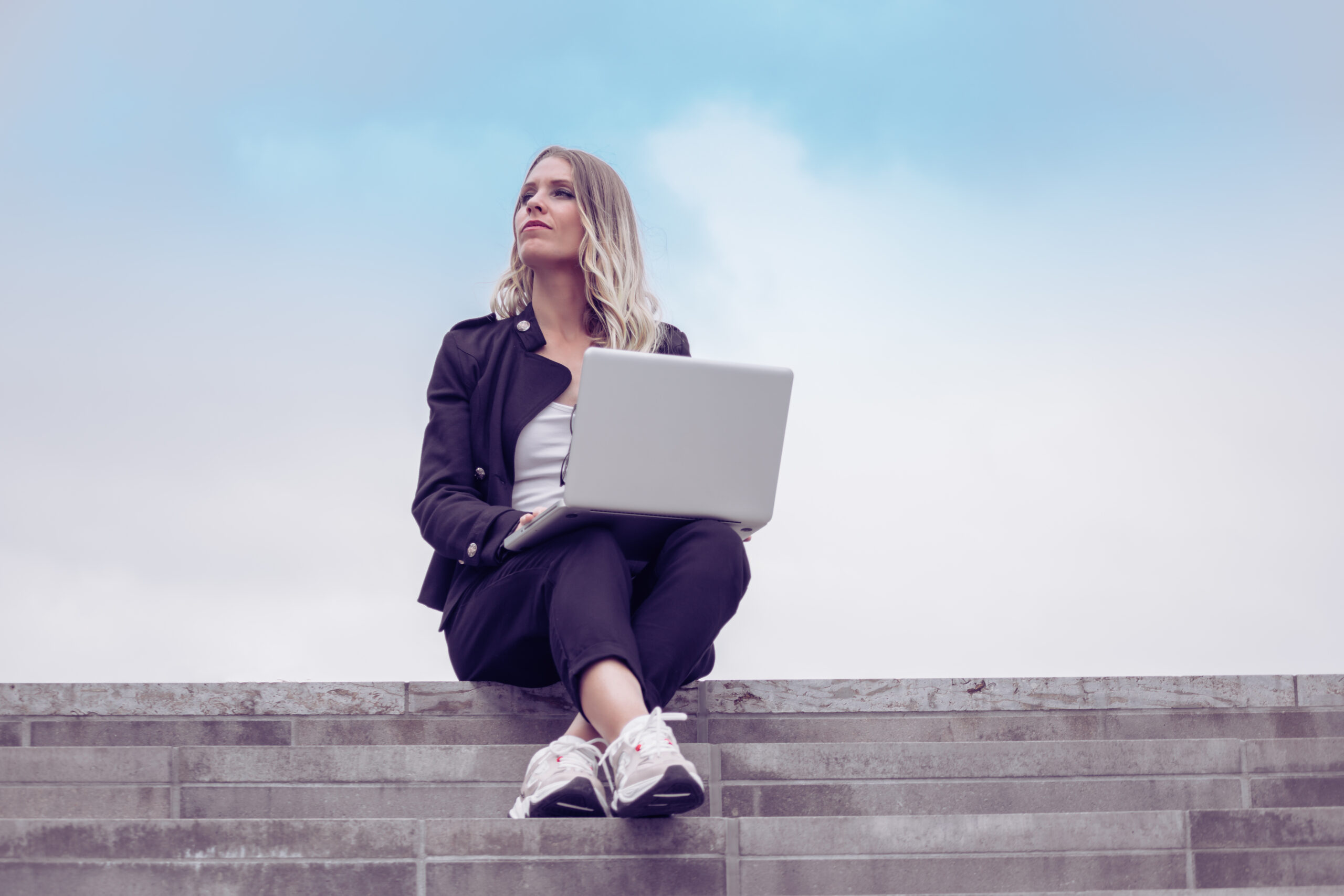 Eine junge Frau arbeitet remote auf ihrem Laptop und schaut mit einem zufriedenen Ausdruck in den Himmel.